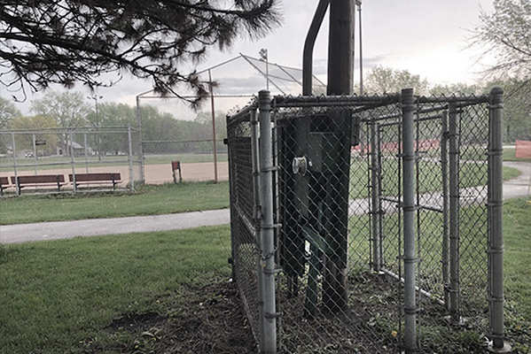 A strut and backboard system surrounded by a chain link fence next to an outdoor baseball field.